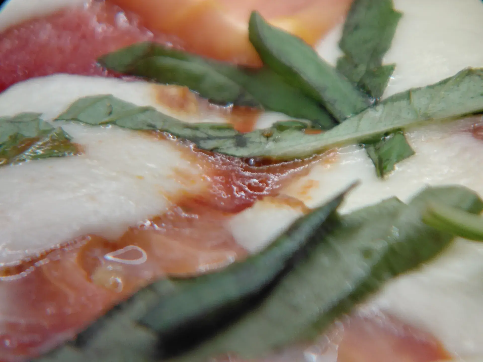 Close-up of fresh mozzarella, tomato, and basil on a Margherita flatbread.
