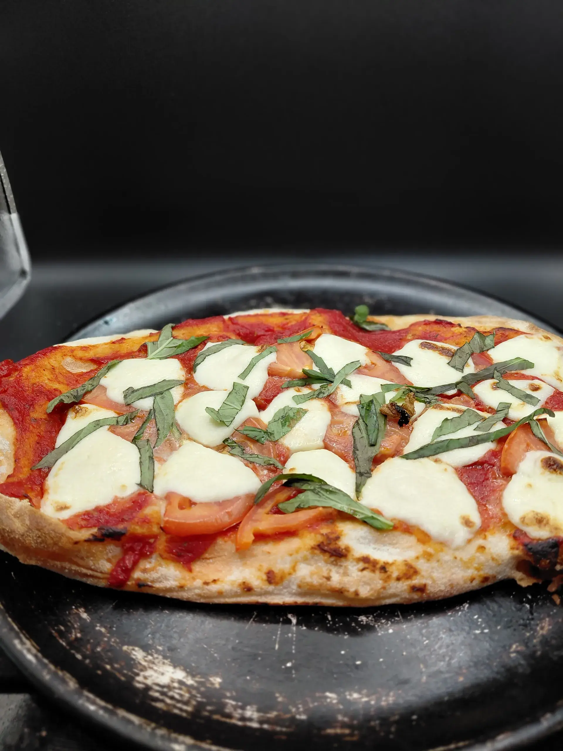 Margherita flatbread with mozzarella, tomato, and basil on a metal tray.